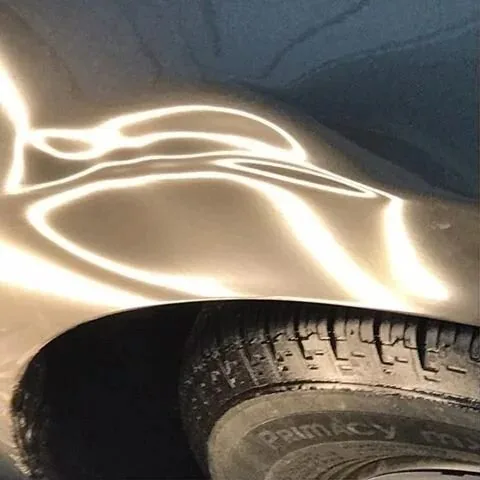 A dented panel under a work light, the dents showing as waves in the reflection
