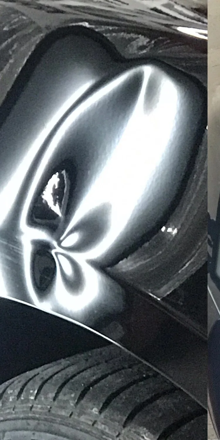 Hail dents picked out across a black panel under a work light