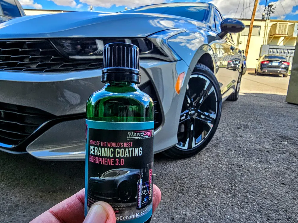 A bottle of NanoPro ceramic coating held in front of a coated car (photo: NanoPro)