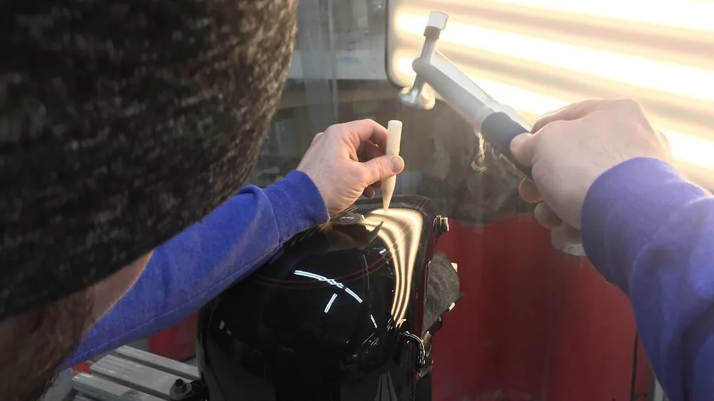 A technician working a dent out from behind the panel with a paintless dent repair rod