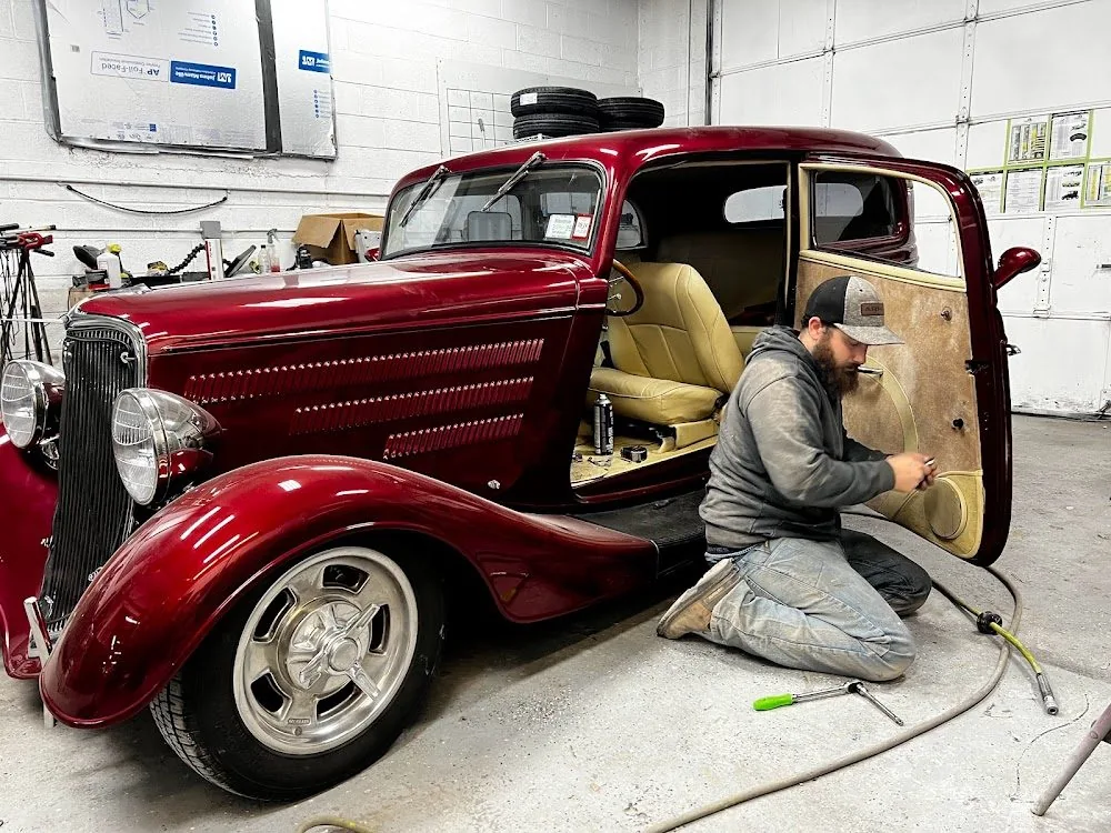 A deep red hot rod on the shop floor with a technician working on the door